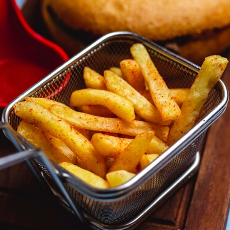 Crispy golden french fries seasoned with spices, served in a metal basket on a wooden surface.