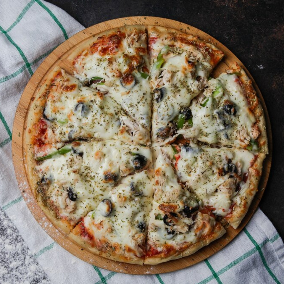 Pizzamore's sliced pizza with melted cheese, olives, and herbs on a wooden board.