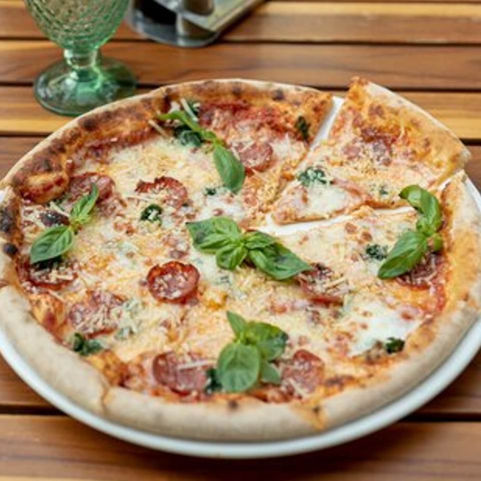 Pizzamore pepperoni pizza with basil and parmesan cheese, with one slice removed, on a wooden table.