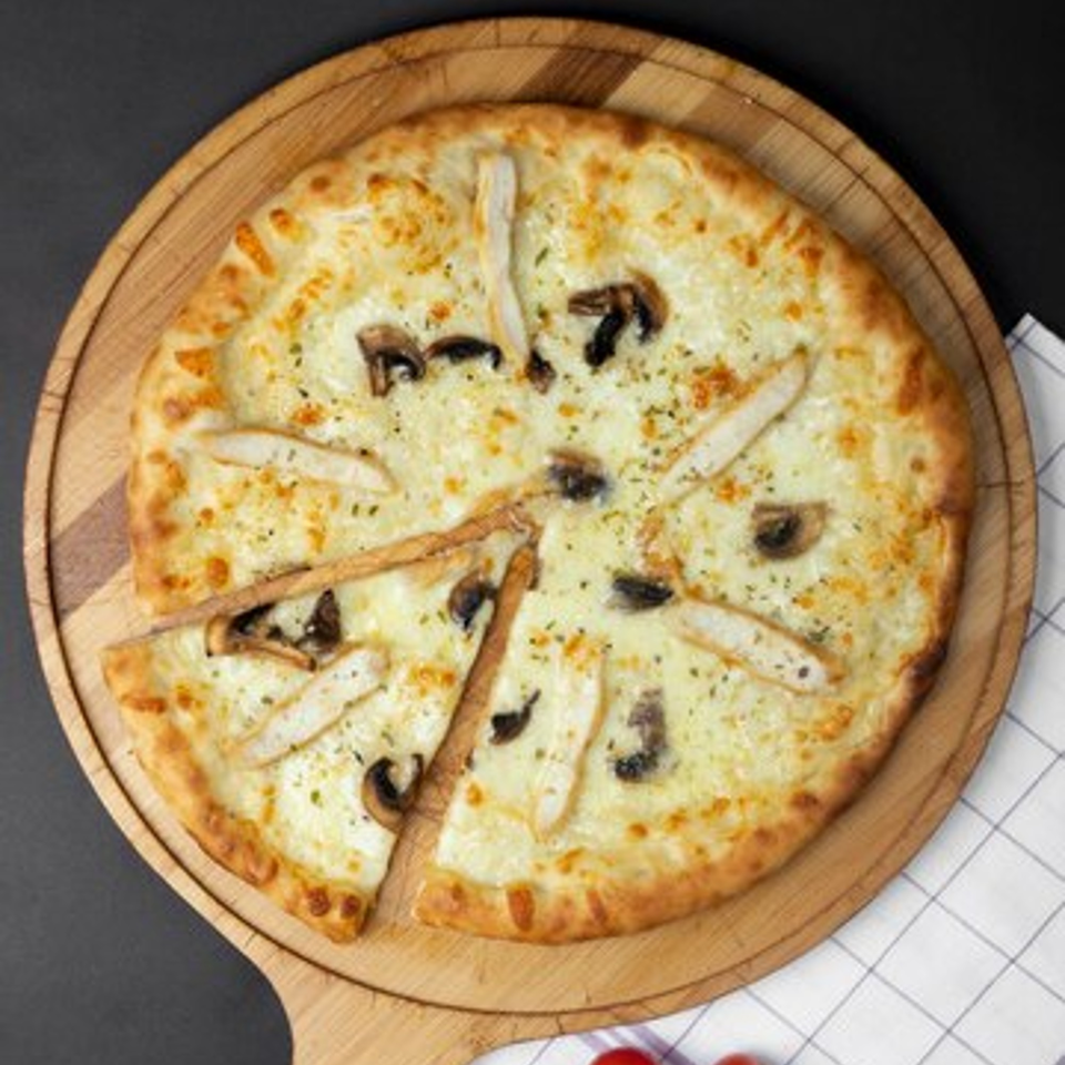 Pizzamore's white pizza with chicken and mushrooms, sliced on a wooden board.