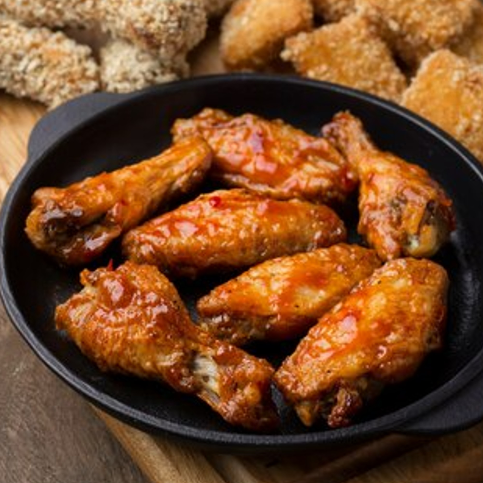 Pizzamore's glazed chicken wings in a black skillet, with crispy chicken nuggets in the background.